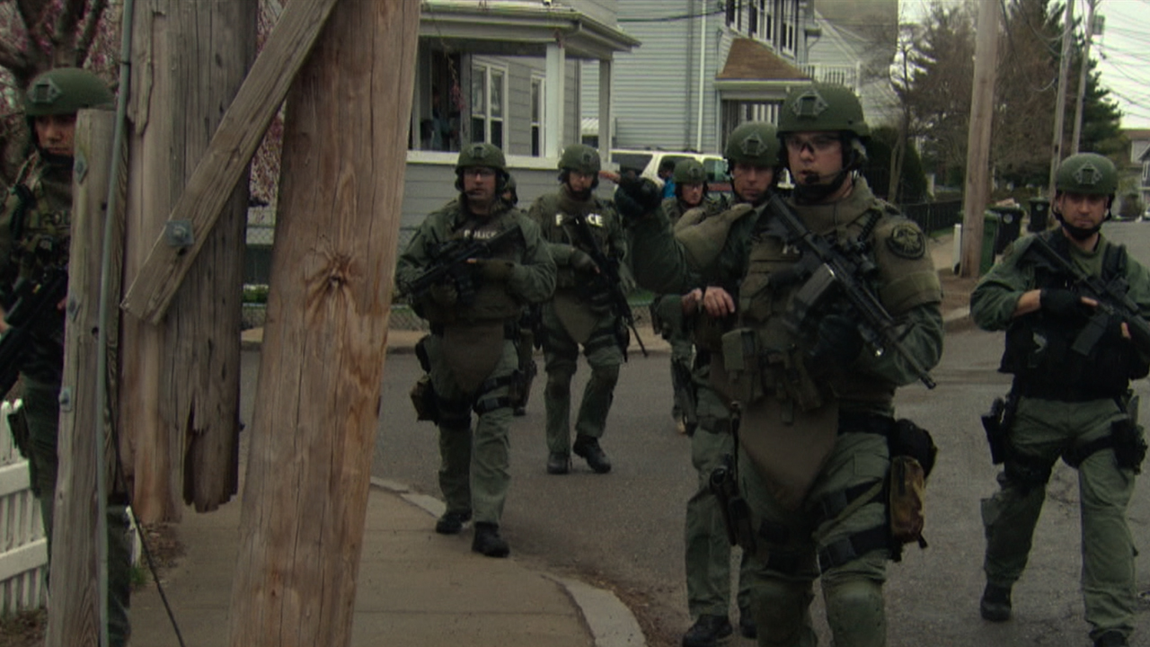 Polícia em pleno funcionamento com armas patrulhando Boston e arredores em uma imagem do bombardeio da Maratona de Boston em American Manhunt.