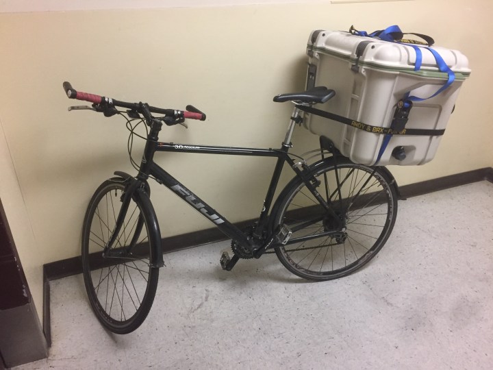 A bicycle with a cooler strapped to the back sits in a lobby.