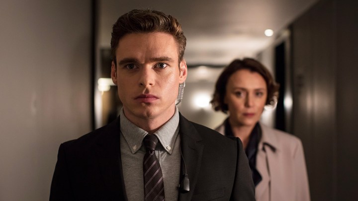 An agent standing in front of a woman, his earpiece in in a scene from Bodyguard.