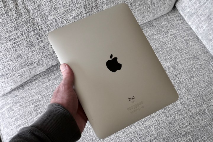 A person holding an original iPad, showing the back.