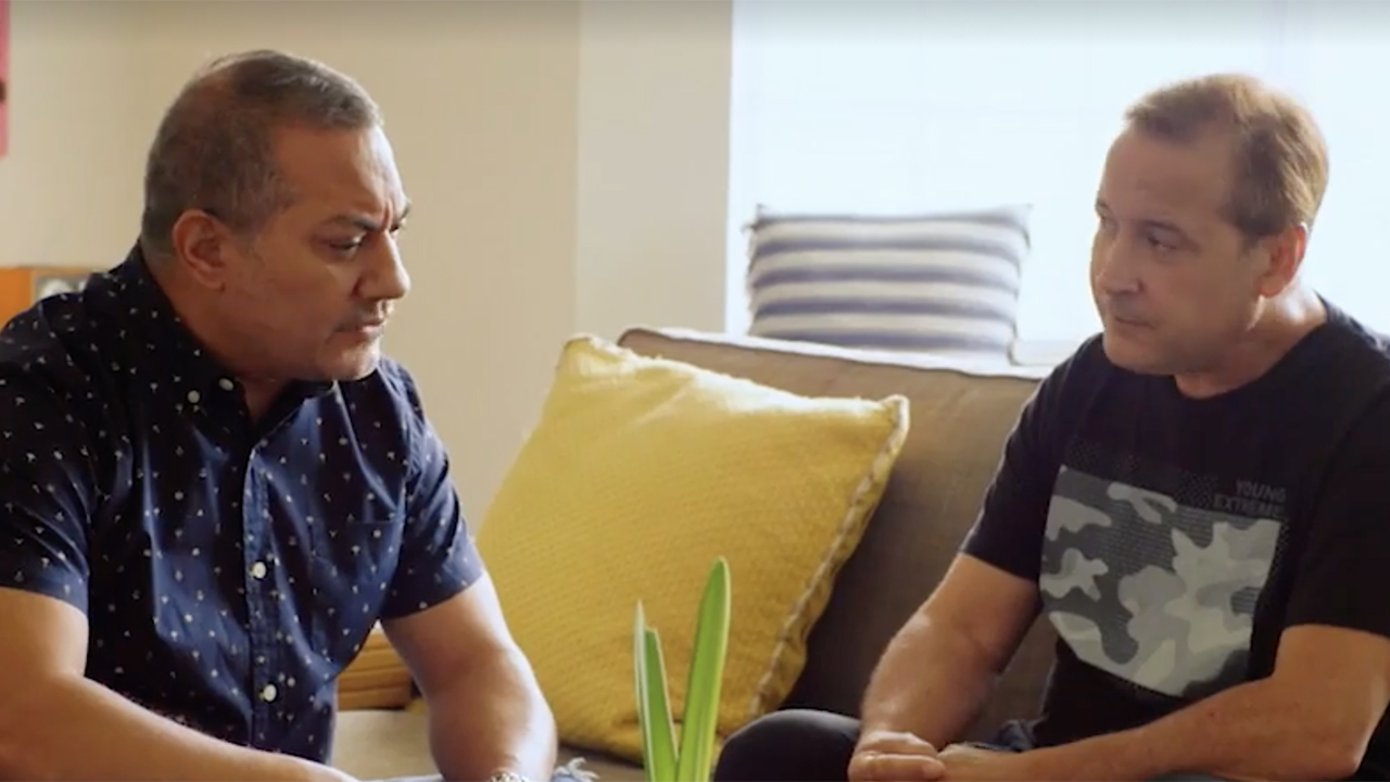 Raul Reyes e Roy Rossello conversando no sofá em cena de Menendez + Menudo: Garotos Traídos.