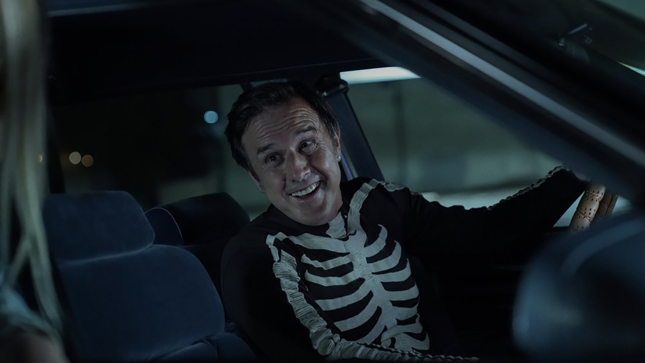 David Arquette como Monty em Mrs. Davis, sentado em um carro vestindo uma camisa esqueleto.