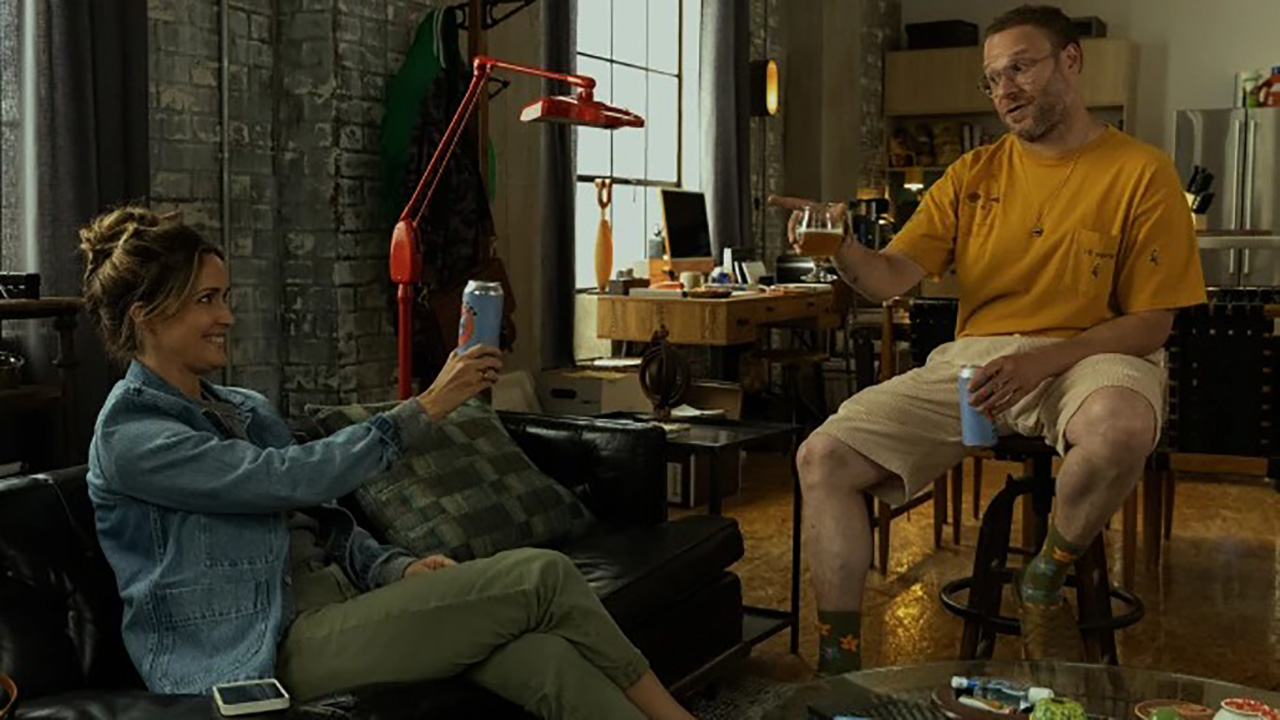 Rose Byrne e Seth Rogen brindam um ao outro sentados em um apartamento em uma cena de Platonic no Apple TV+.