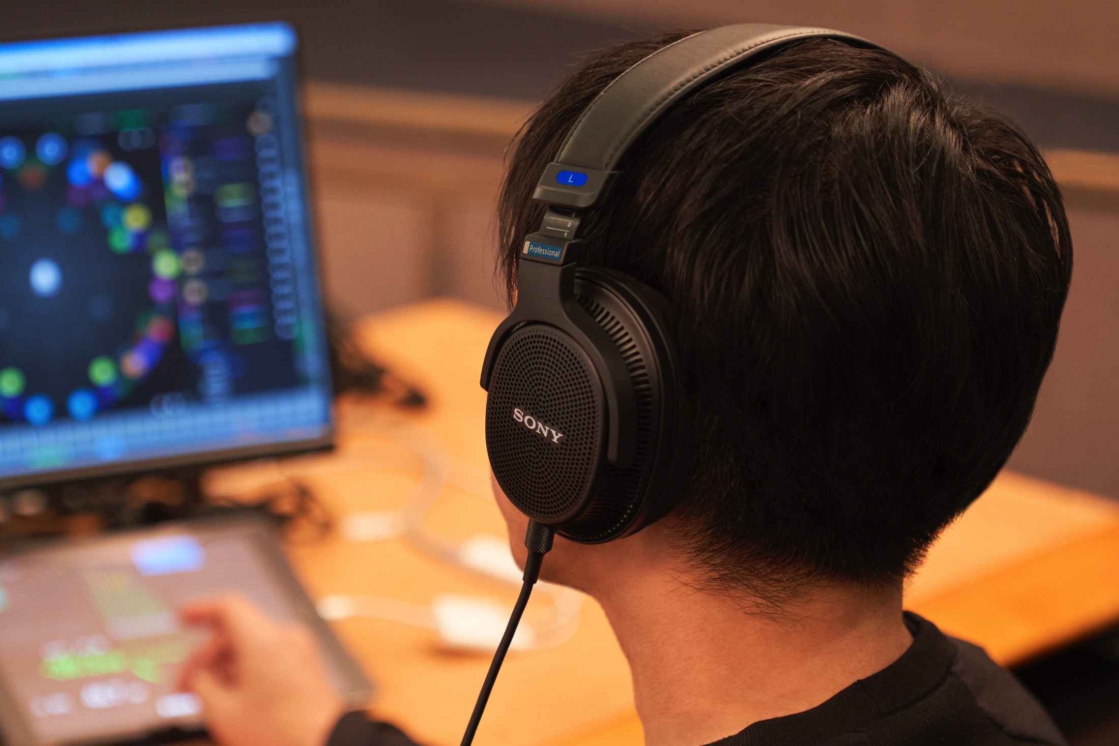 Homem usando fones de ouvido Sony MDR-MV1 abertos enquanto mixa áudio.