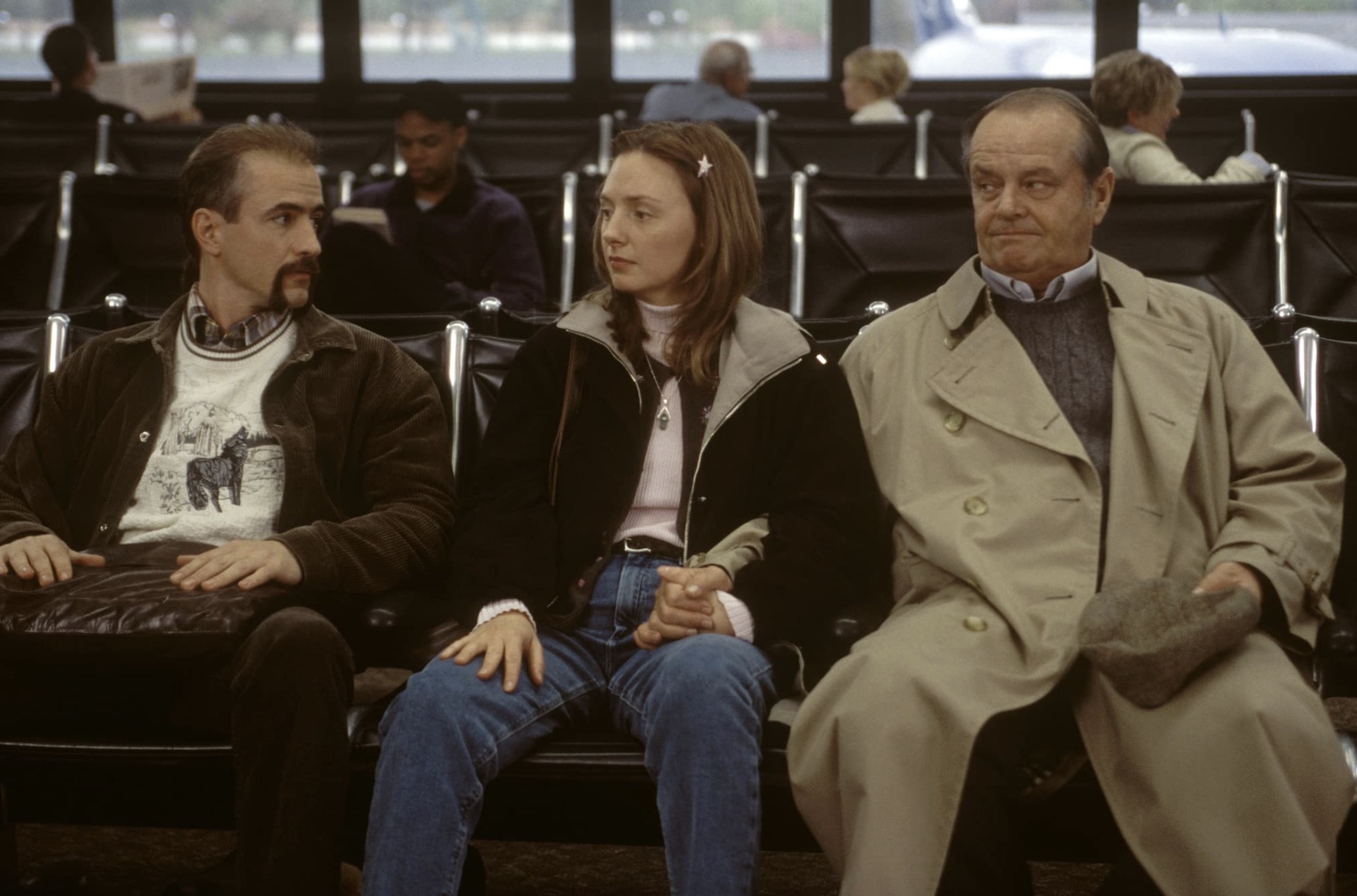 Três pessoas sentam-se lado a lado no aeroporto.