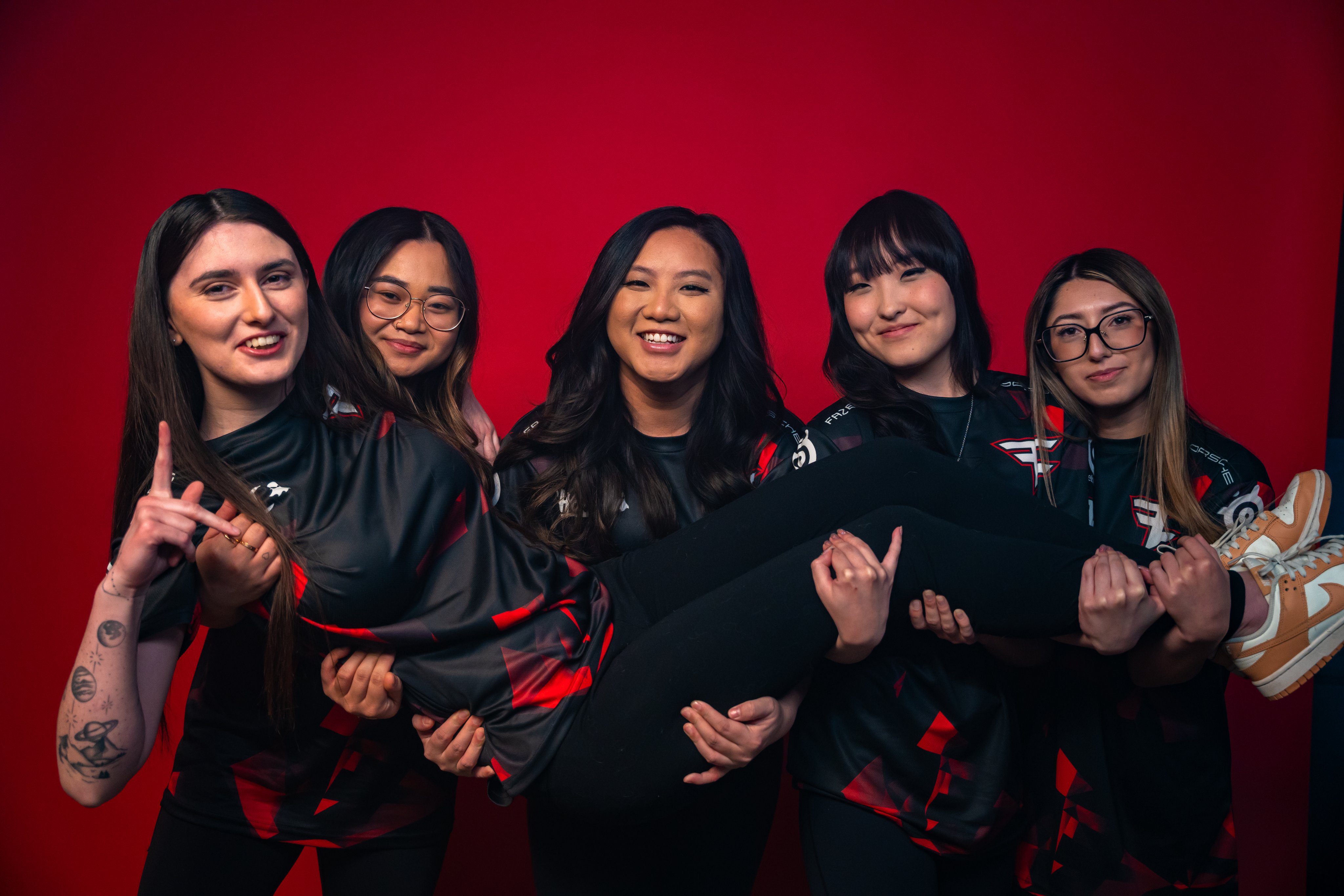 A team photo of all five members of FaZe Clan's first all woman esports team. Four of the members are holding up the fifth member and everyone is smiling.