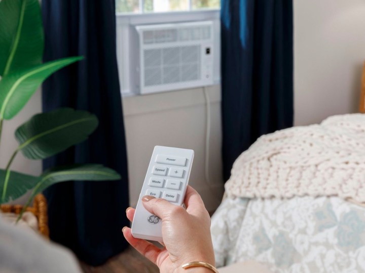 A hand holds a remote and controls the GE 5,000 BTU window air conditioner.