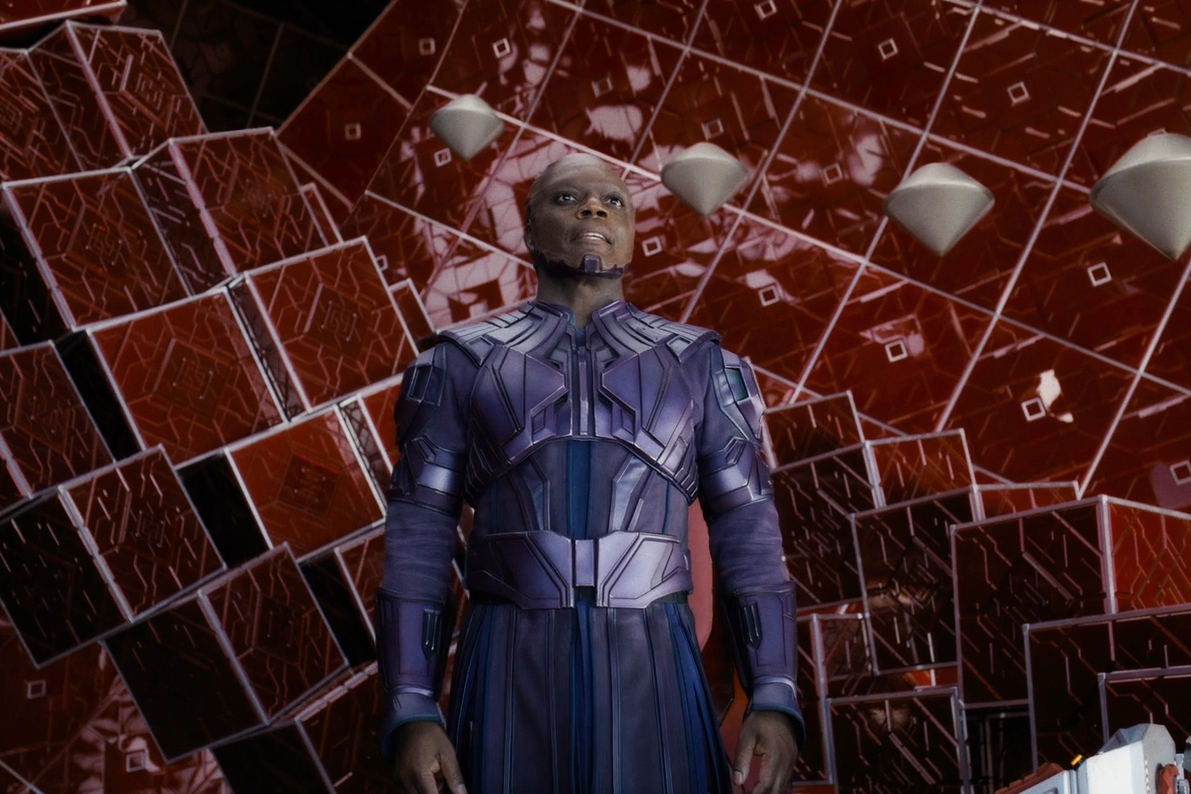 O Alto Evolucionário se levanta em uma sala de paredes vermelhas em Guardiões da Galáxia Vol.  3.