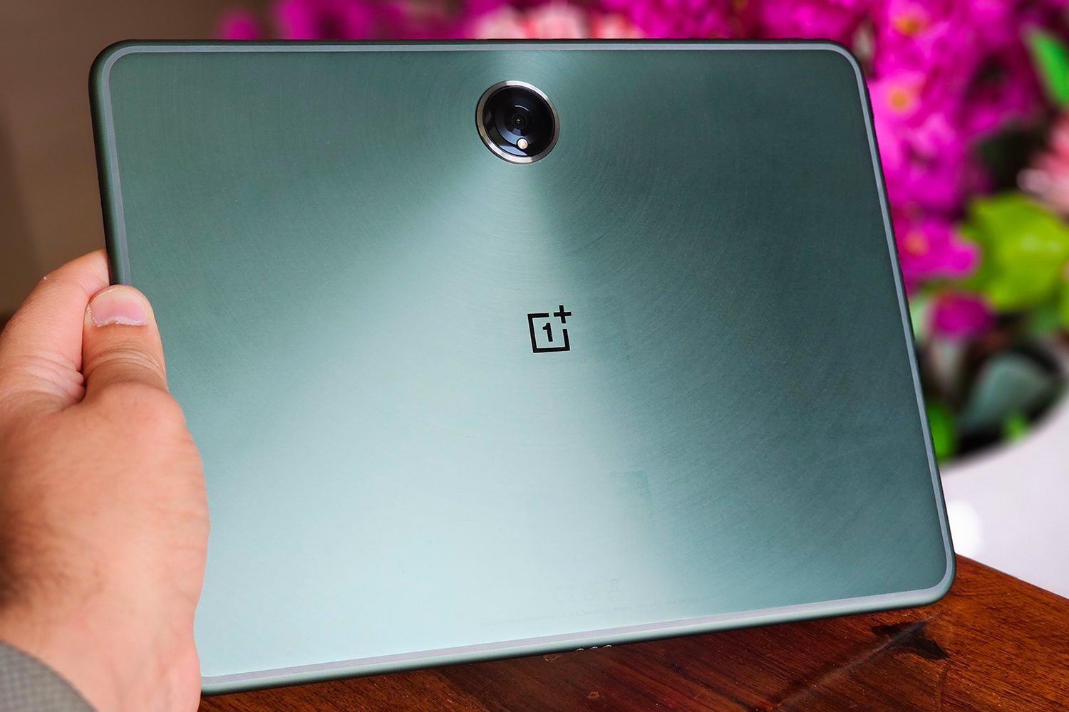 OnePlus Pad Android tablet in green color with pink artificial floweres and wooden tablet in the background. 