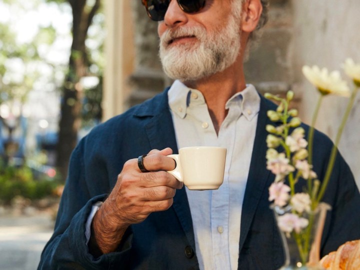 A man wears an Oura Ring Gen3 while drinking coffee at a cafe.