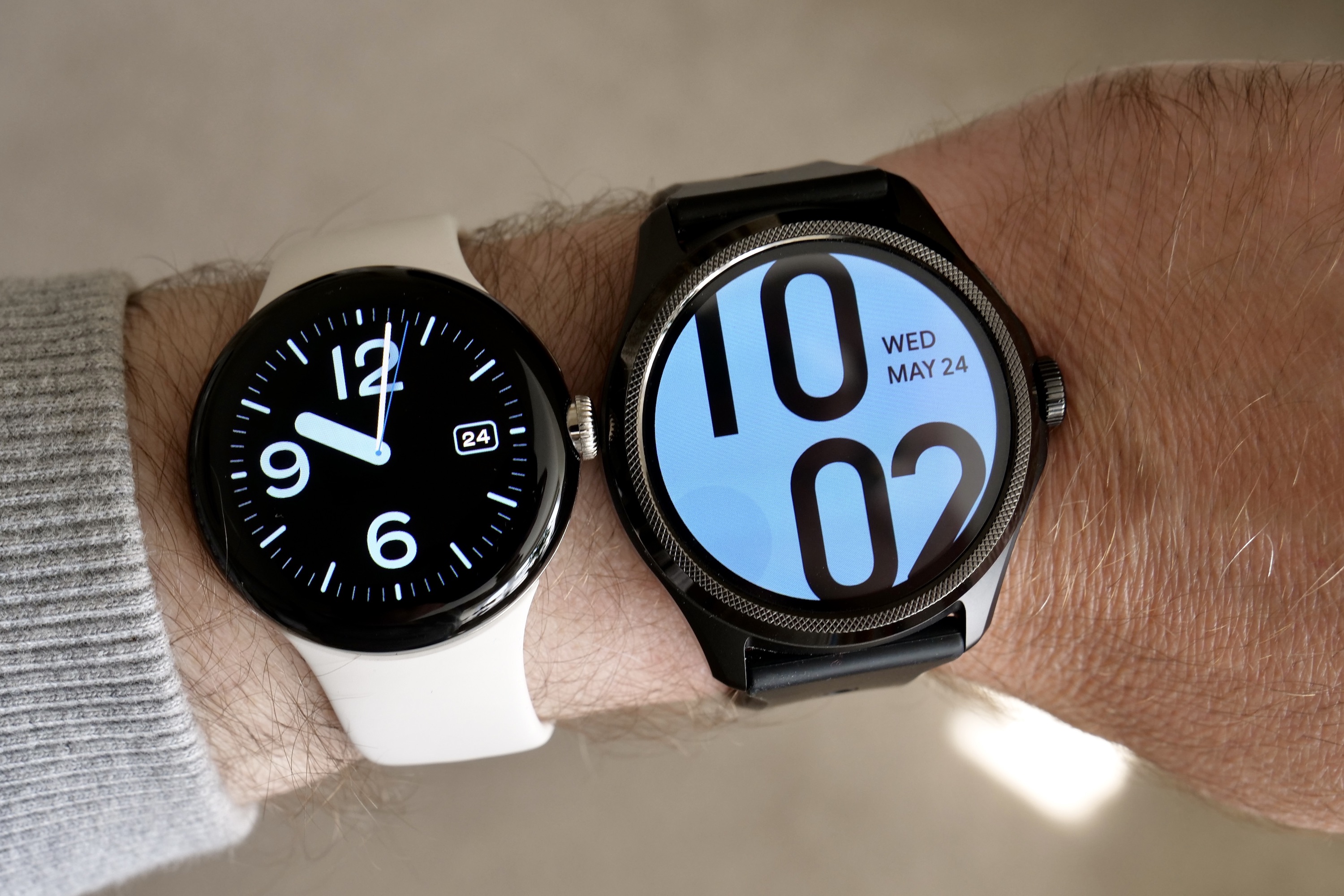 A Pixel Watch and TicWatch Pro 5 side-by-side on a person's wrist.