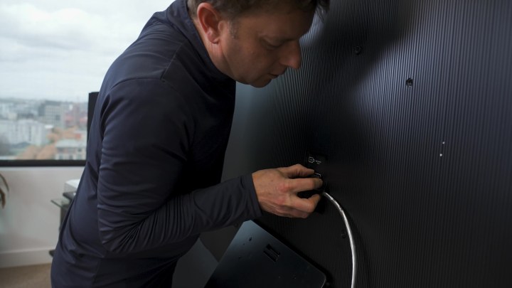 A man plugs a cable into the One Connect box on a Samsung S95C OLED TV.