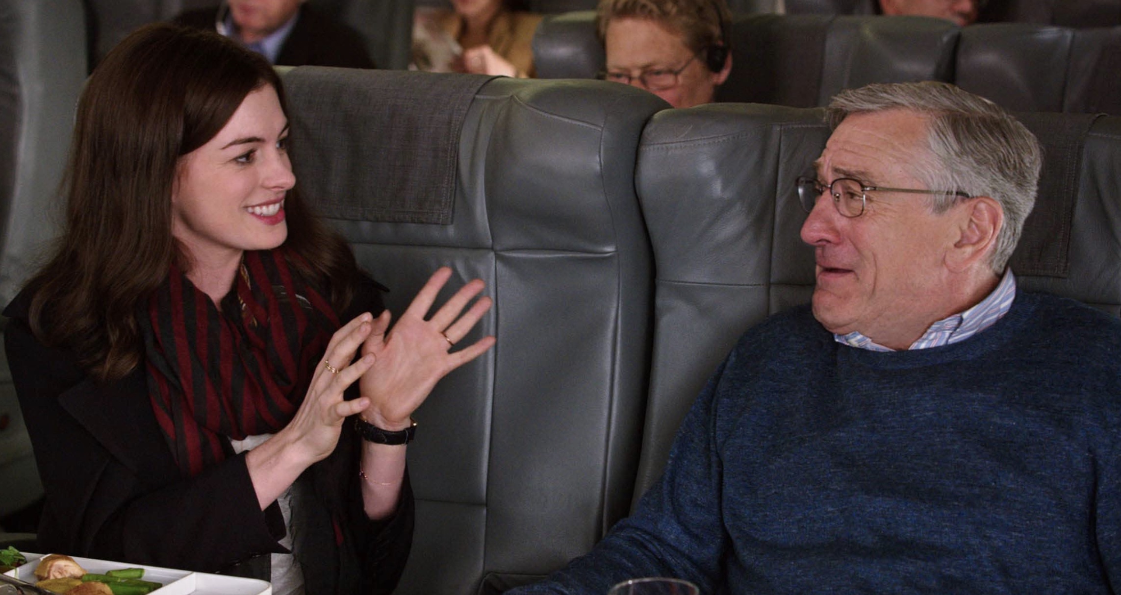 Anne Hathaway senta ao lado de Robert De Niro em um avião.