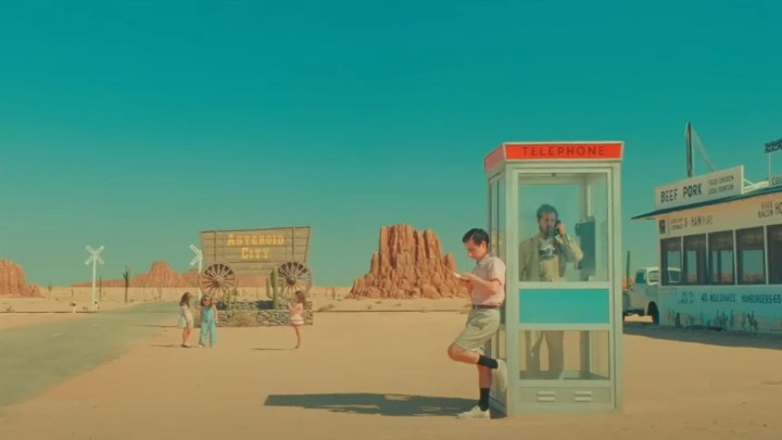 A boy leans against a telephone booth in Asteroid City.