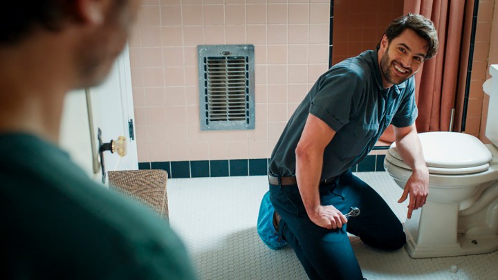 Tom kneeling in front of the toilet smiling in a scene from Based on a True Story.