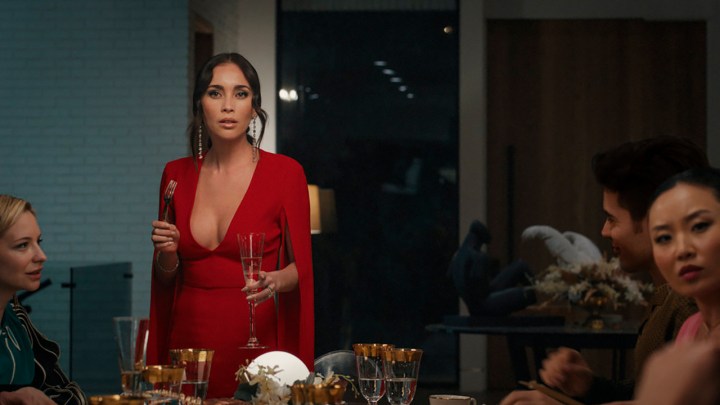 Ruby in a red dress at a dinner table in a scene from Based on a True Story.