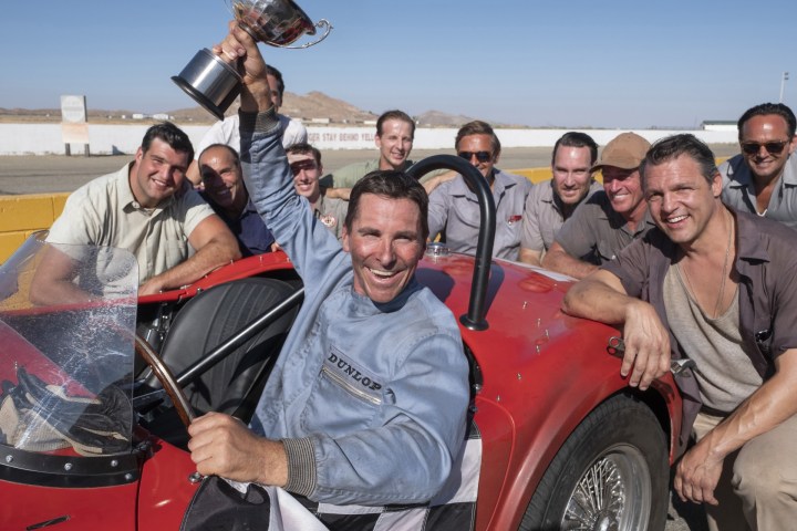 A man holds a trophy while in a red car in Ford v Ferrari.
