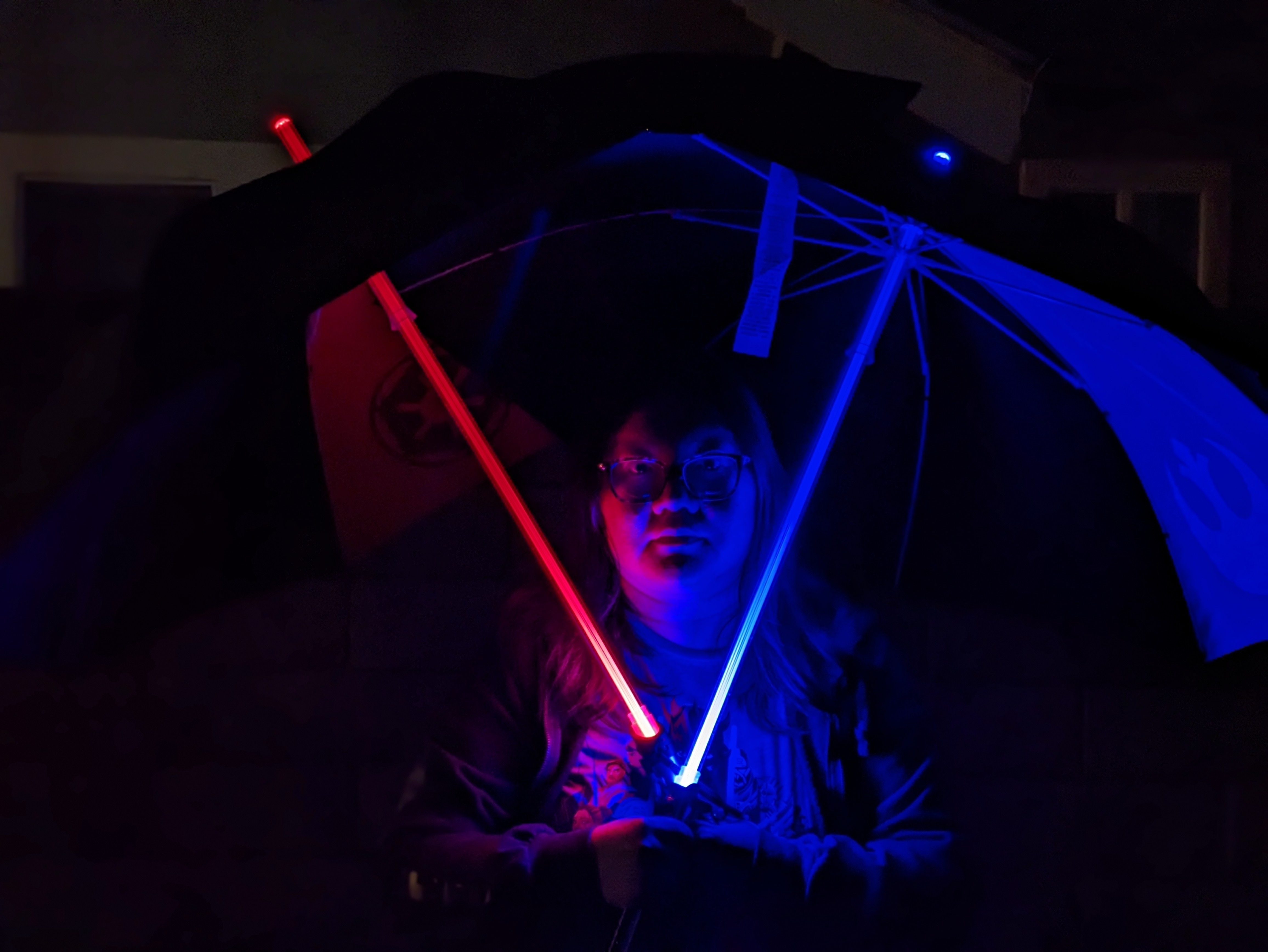Night portrait mode photo of Christine holding lightsaber umbrellas taken with Google Pixel 7a