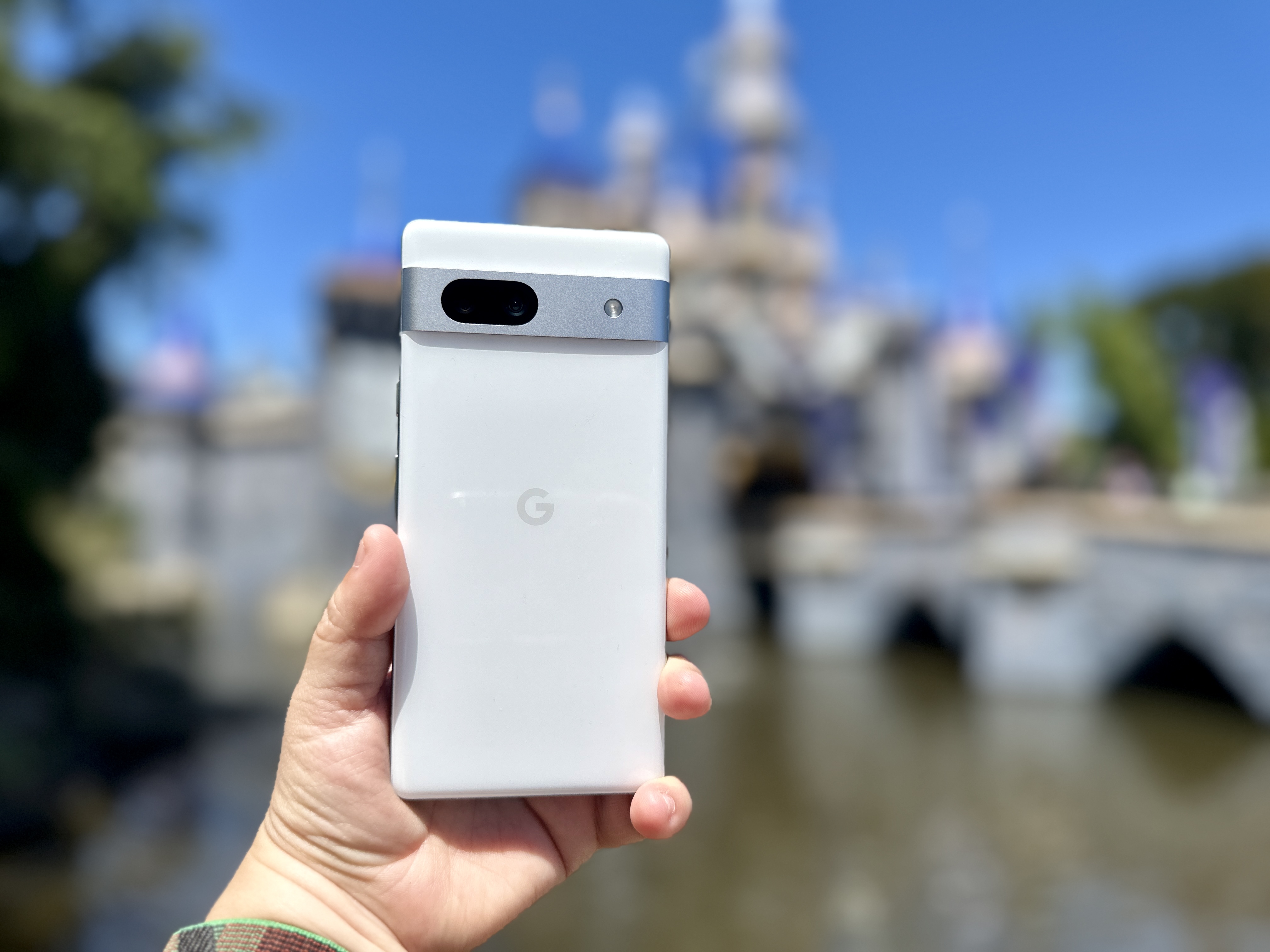Google Pixel 7a held in hand in front of Disneyland castle