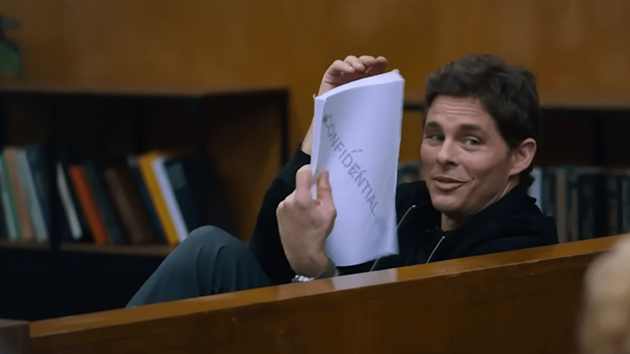 James Marsden sentado no tribunal, mostrando a todos um roteiro que está lendo em Jury Duty.