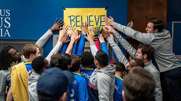 The team with their hands on the Believe poster in a scene from Ted Lasso.