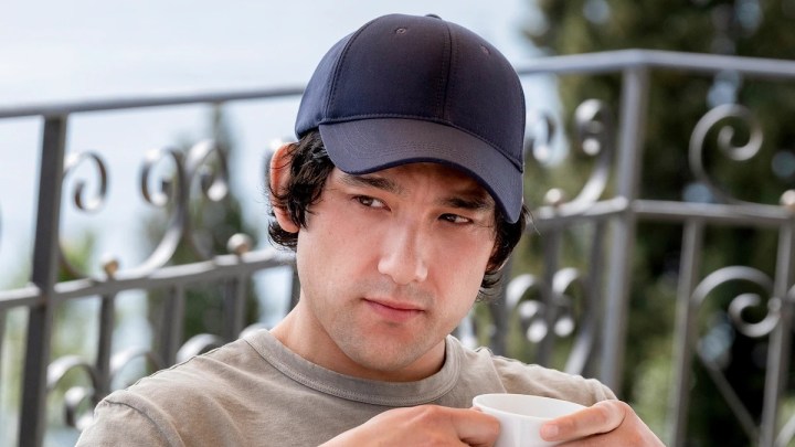 Ethan wears a hat and sips his coffee in The White Lotus.