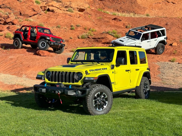 Three Jeep Wrangler 4xe SUVs on grass and dirt.