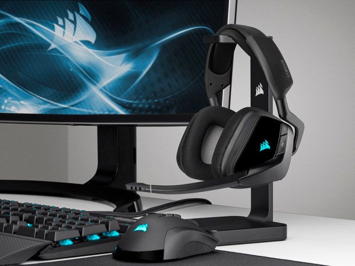 The Corsair Void RGB Elite gaming headphones on a rack next to a gaming PC.