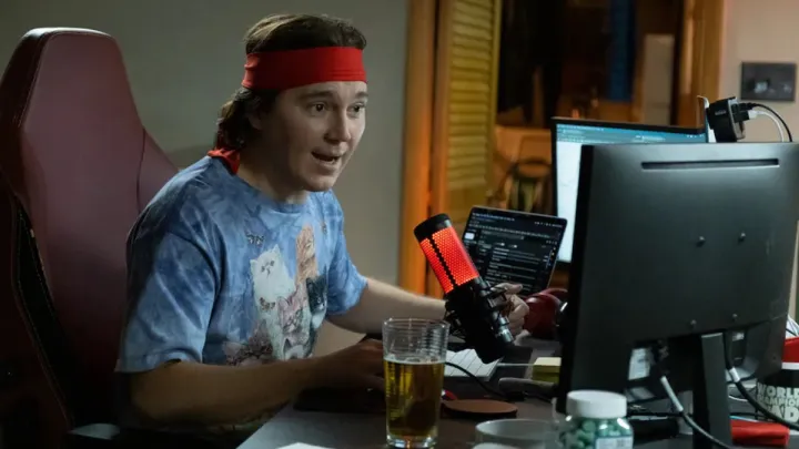 Paul Dano se sienta detrás de un micrófono en Dumb Money.