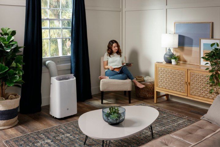 O ar condicionado portátil GE 10.000 BTU resfria uma sala de estar enquanto uma mulher lê.