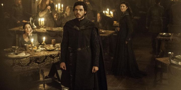 Robb Stark standing before someone while his mother stands behind him in Game of Thrones.