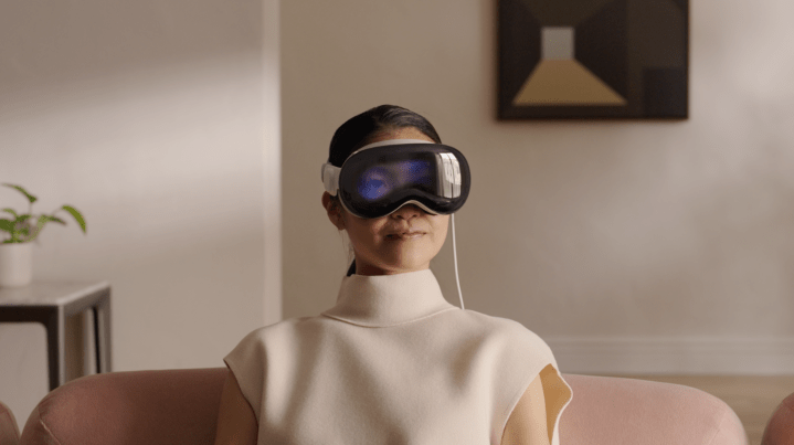 A woman wears the Apple Vision Pro headset while sitting on a couch.