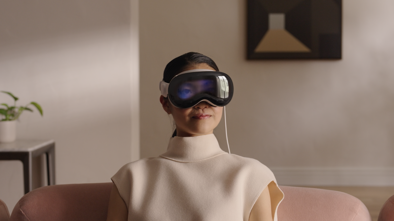 A woman wears the Apple Vision Pro headset while sitting on a couch.