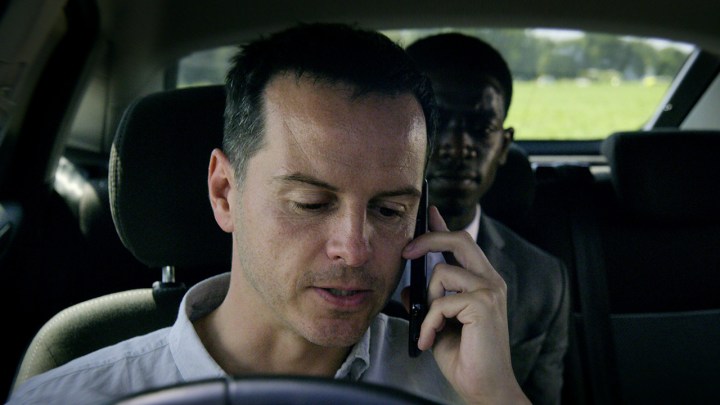 Um homem no banco do motorista de um carro está ao telefone, um jovem no banco atrás dele no episódio Smithereens de Black Mirror.