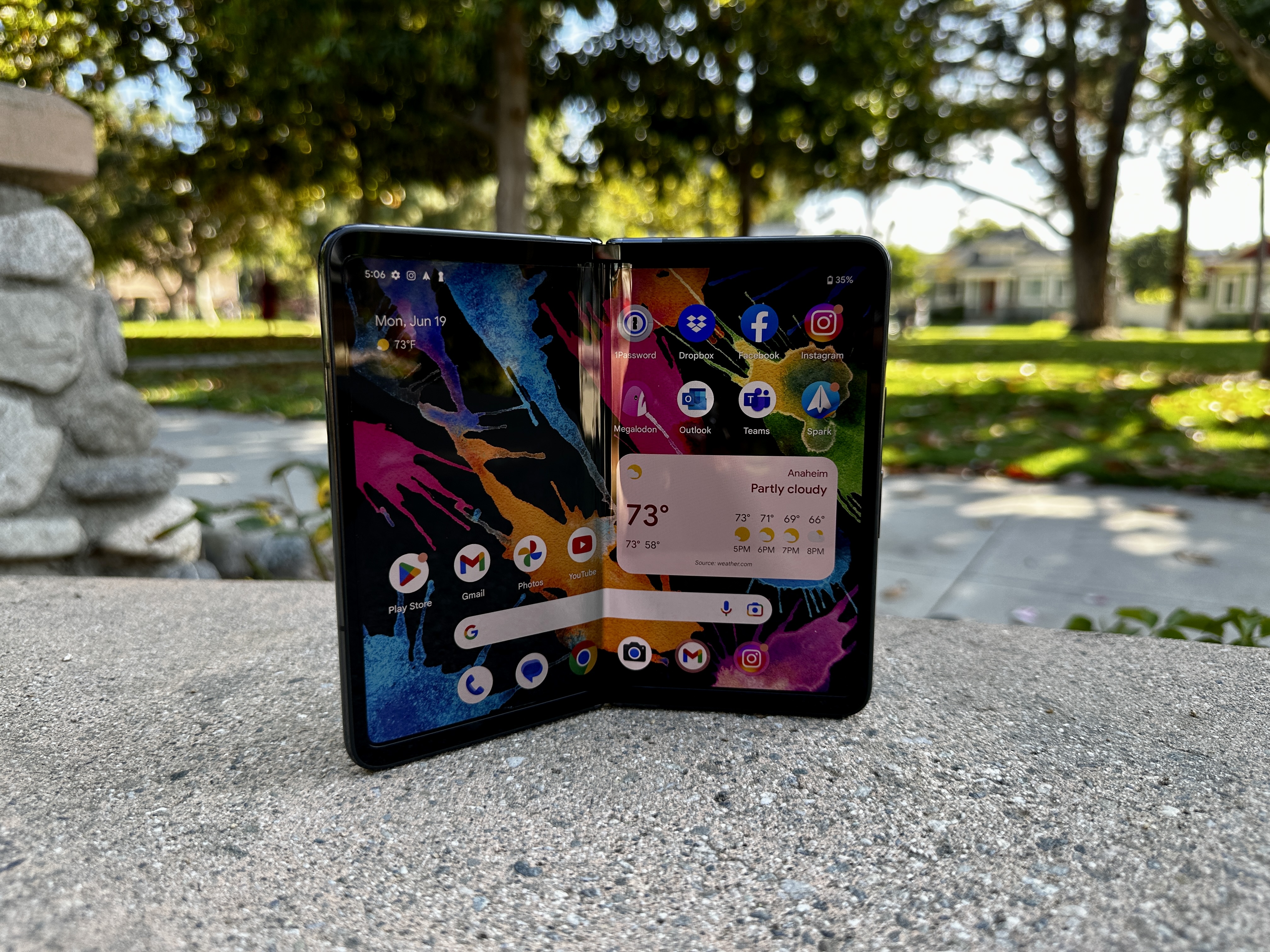 Google Pixel Fold em Obsidian ligeiramente aberto no banco do parque.