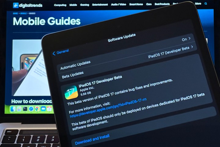 iPad showing iPadOS 17 Developer Beta 1 update screen with MacBook in the background.