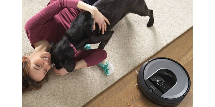 O iRobot Roomba i8+ sendo usado em uma sala de estar ao lado de uma mulher e seu cachorro.