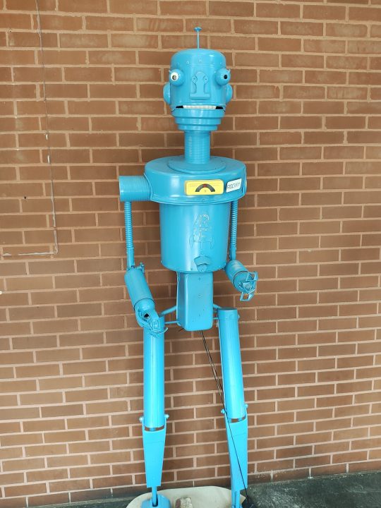Un robot blu in piedi contro un muro di mattoni, ripreso con il Motorola Razr Plus.