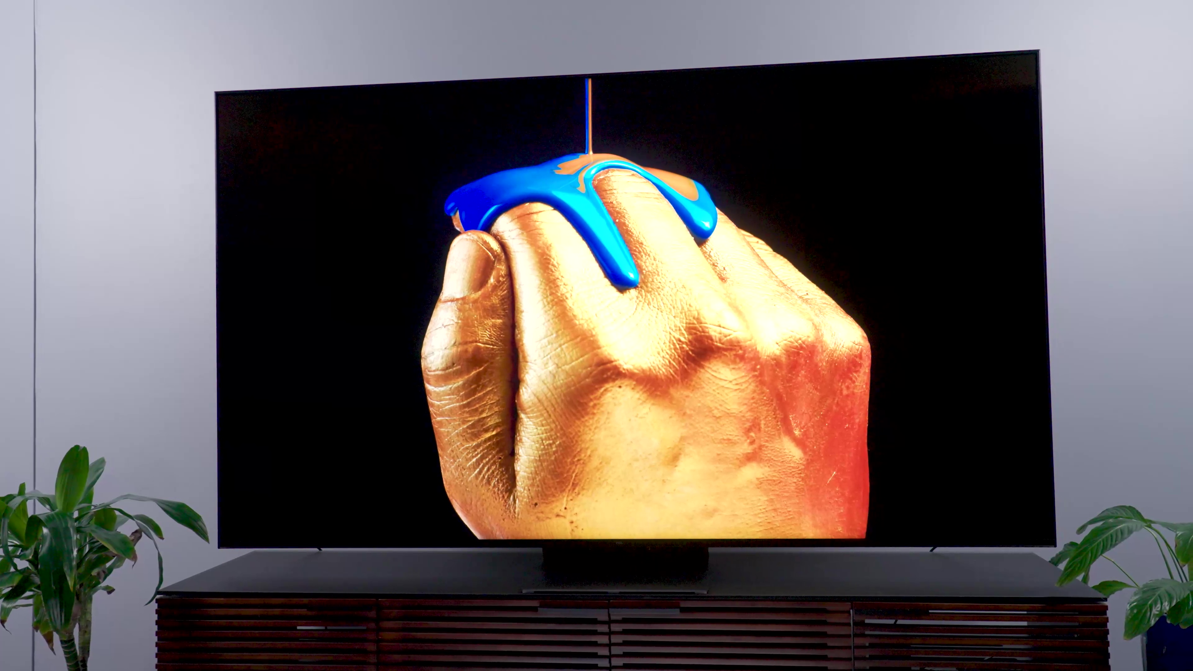 A stylized image of metallic blue paint being poured over hand shown on a a TCL QM8.