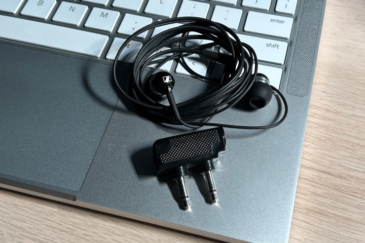 Um conjunto de fones de ouvido com fio Sennheiser vistos com um adaptador de viagem de avião, sobre o teclado de um laptop.