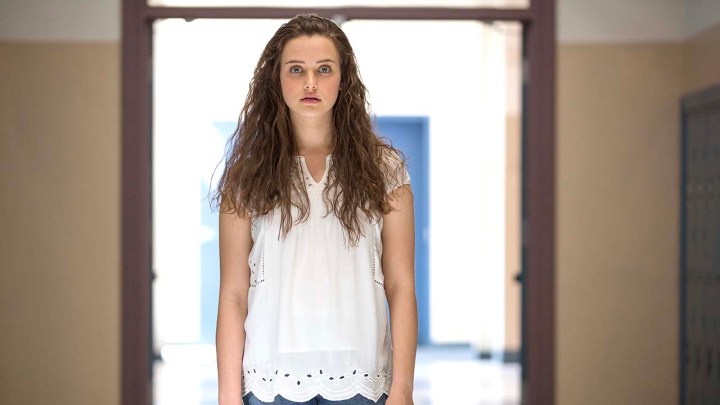 Hannah from 13 Reasons Why wearing a white shirt, standing with a white light behind her.