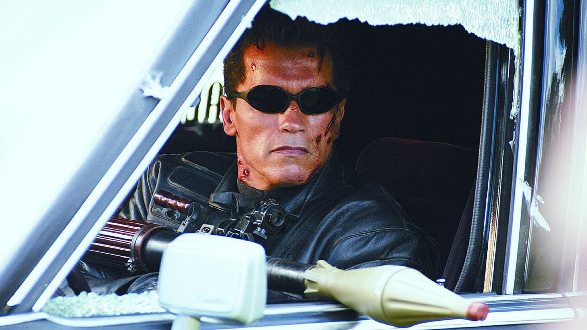 Arnold Schwarzenegger aims a rocket launcher out of a car window.