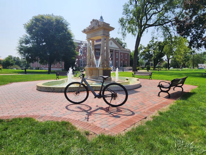Velotric T1 e-bike parked in front of a fountain on a town green.