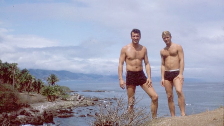 Rock Hudson stands with a shirtless male on a cliff in Rock Hudson: All That Heaven Allowed.