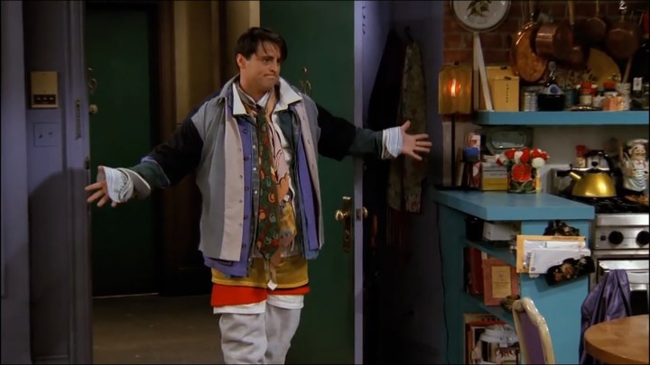 Joey standing at the door of Monica's apartment wearing layers and layers of clothing, his arms spread wide in a scene from Friends.