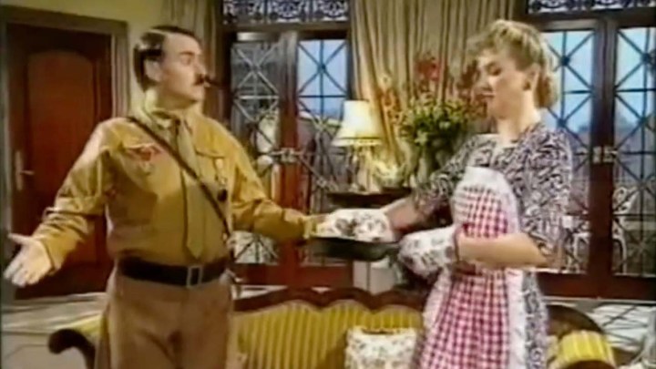 An actor dressed as Hitler talking to his wife in a sitcom-like home scene in the show Heil Honey I'm Home!