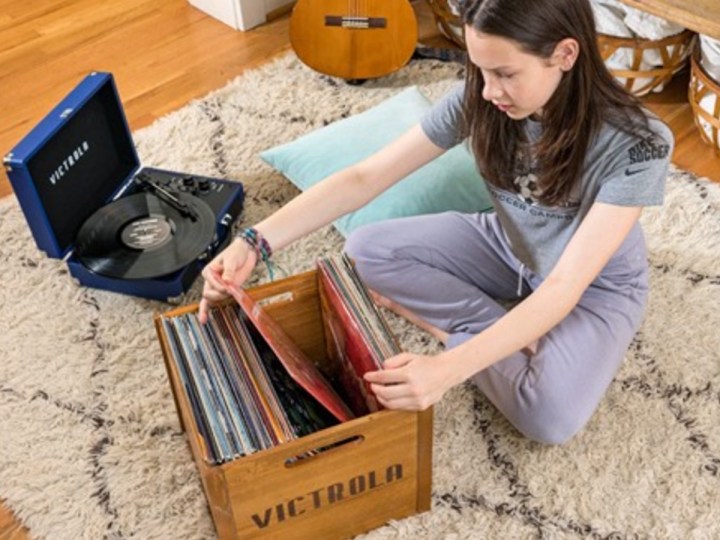 A teenager looks through records on the floor next to a Victrola Bluetooth portable record player.