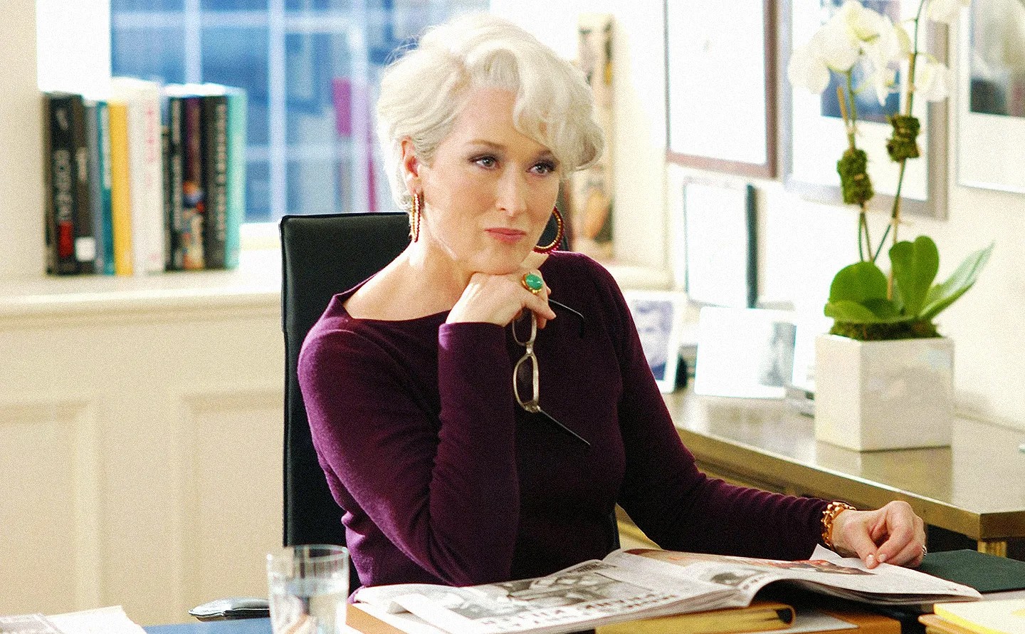 Meryl Streep está sentada em uma mesa em O Diabo Veste Prada.