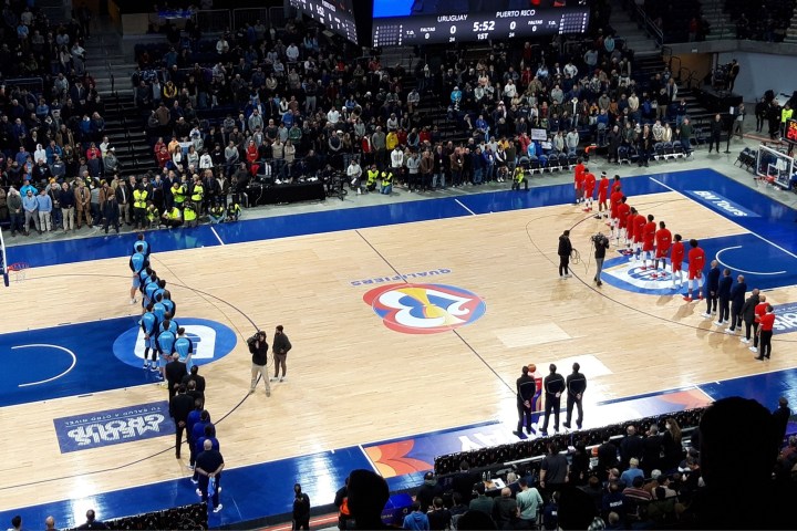 Basketball players stand on opposite sides of the court.