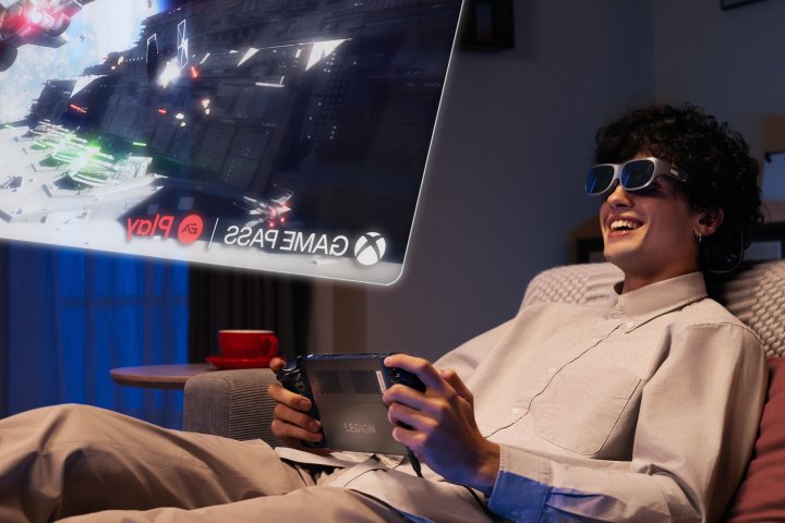 A closeup of a person reclining on a sofa, playing a game on Lenovo Legion Go while looking up at a virtual screen in Legion glasses.